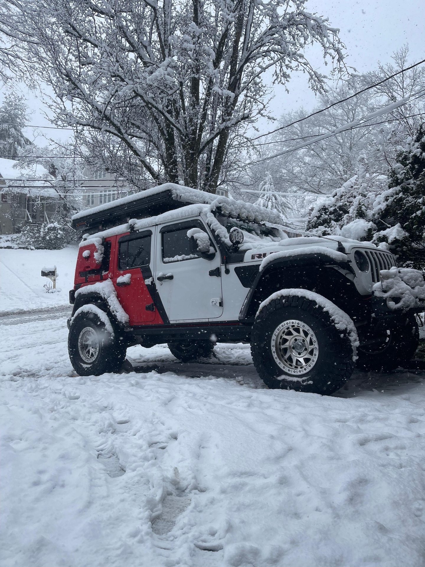 Red and white Jeep Wrangler with roof tent in deep snow